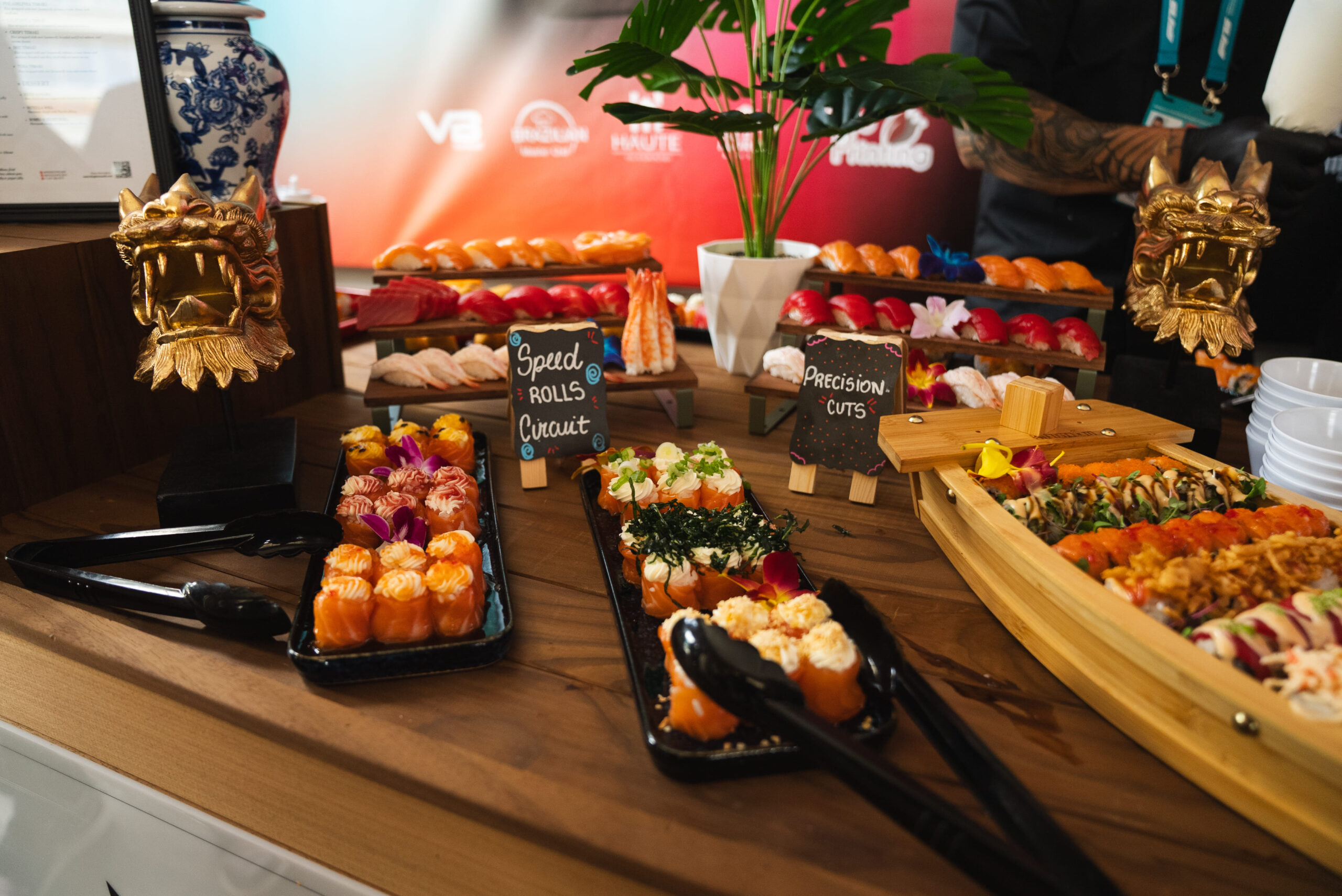 A display of assorted sushi rolls and sashimi arranged on black trays and a wooden boat. Small chalkboard signs read Special Rolls & Circuit and Precision Cuts. Decorative ornaments and a plant are in the background.